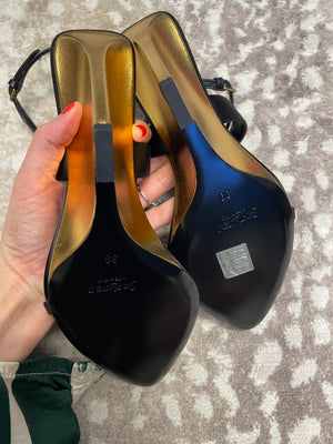 Black high-heeled shoes with gold soles held by a hand on a textured surface
